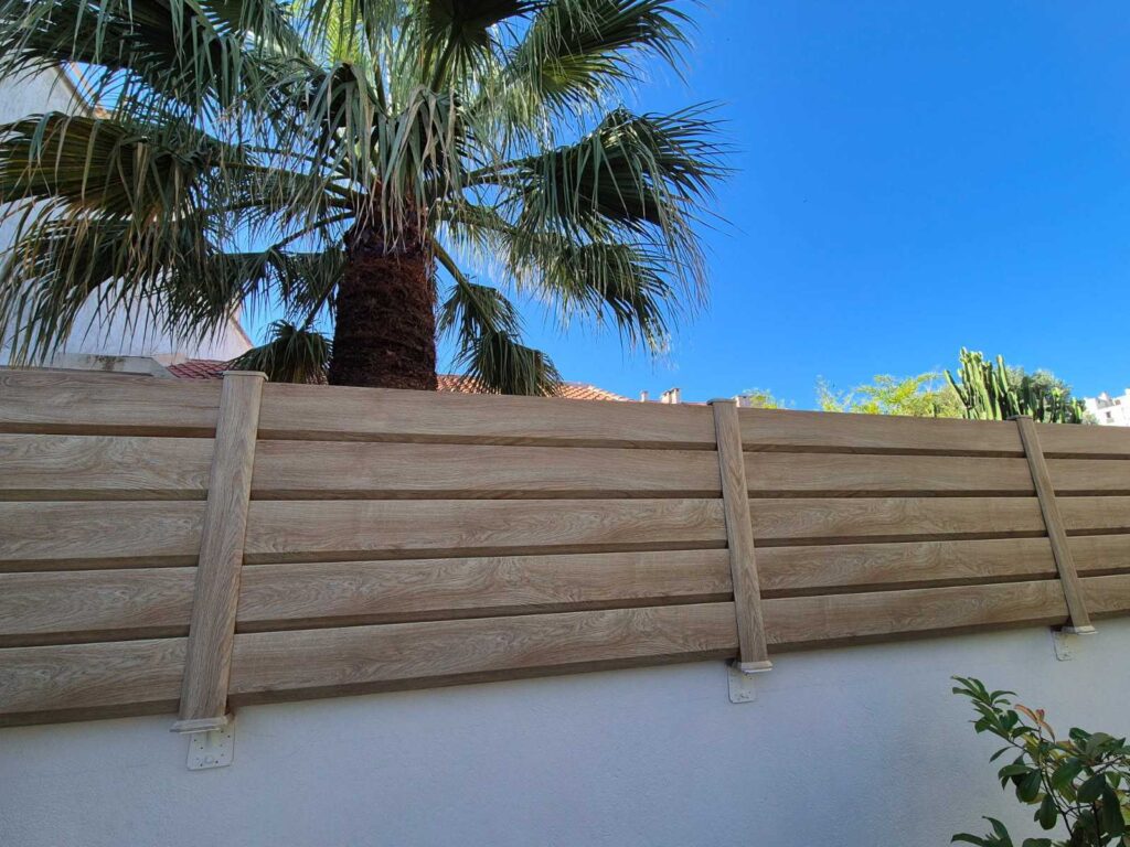 La clôture persienne aspect bois Closea Woodec Malt est installée contre un muret.